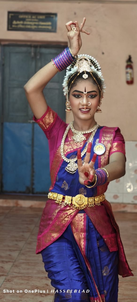 Full solo classical dancer standing in orange and gold silk costume with temple crown